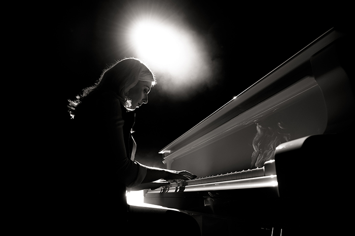 Black and white photo of woman playing piano with spot light feat