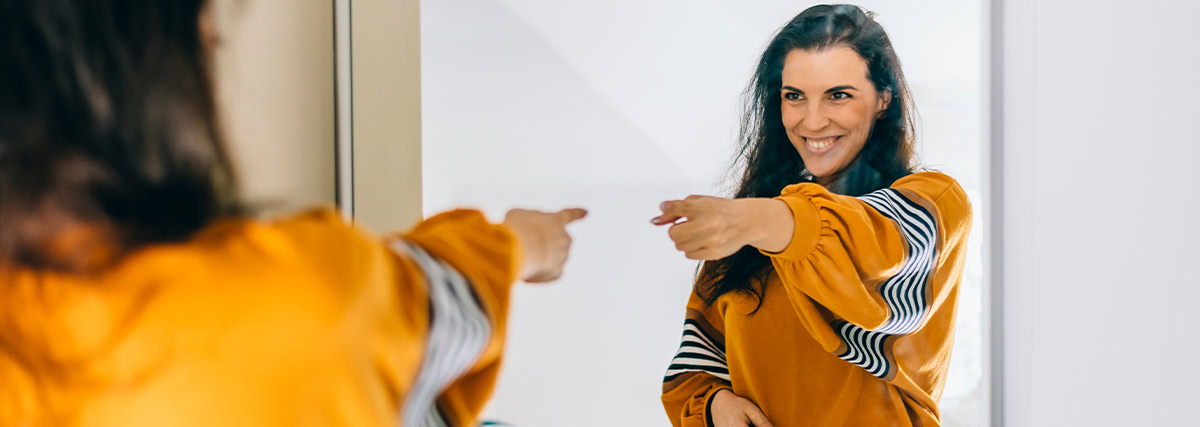 Confident woman pointing finger at reflection in mirror
