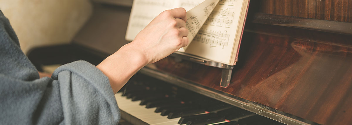 Hand of a woman turning music sheet to the next page at a piano