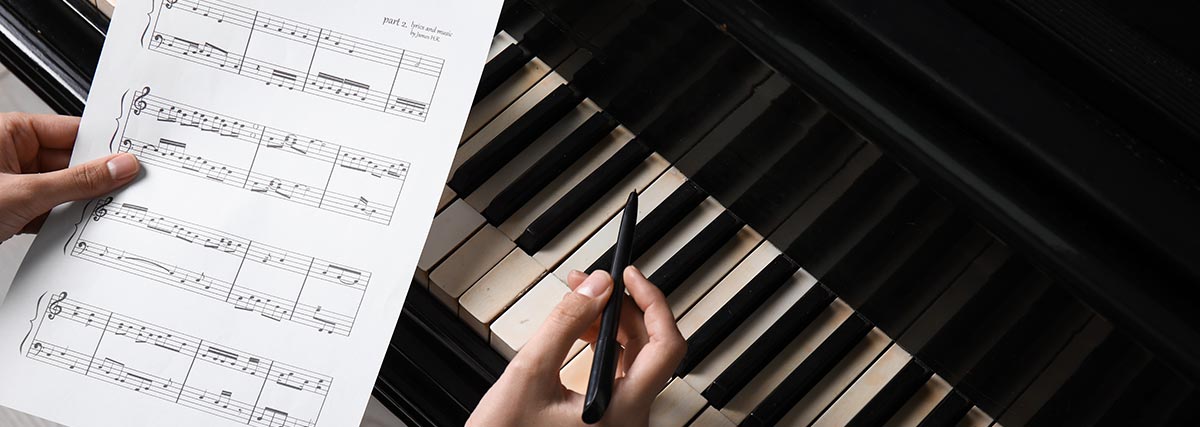 Hands holding sheet music and pen at a piano