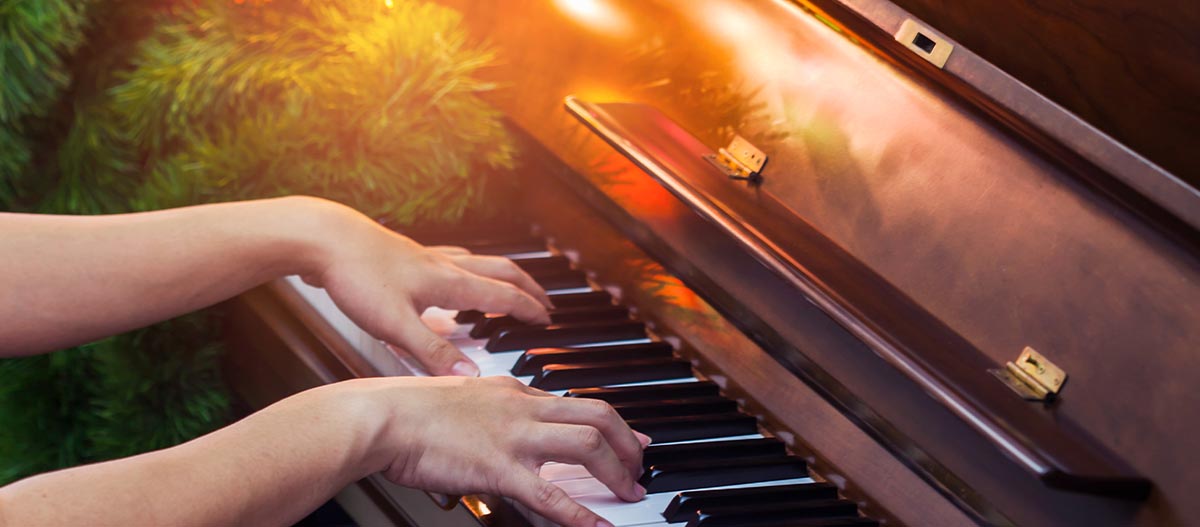 Hands playing piano with Christmas tree in the background