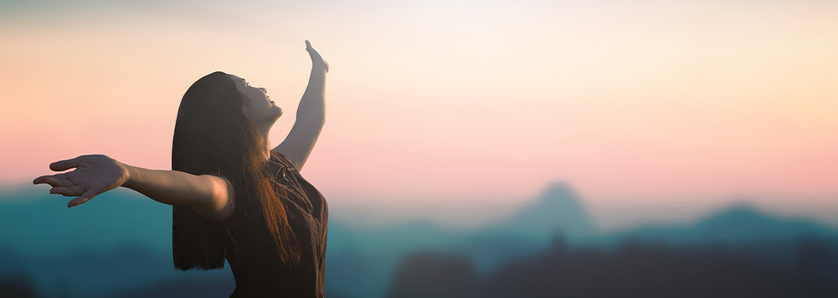Happy woman raised hands on blurred mountain background