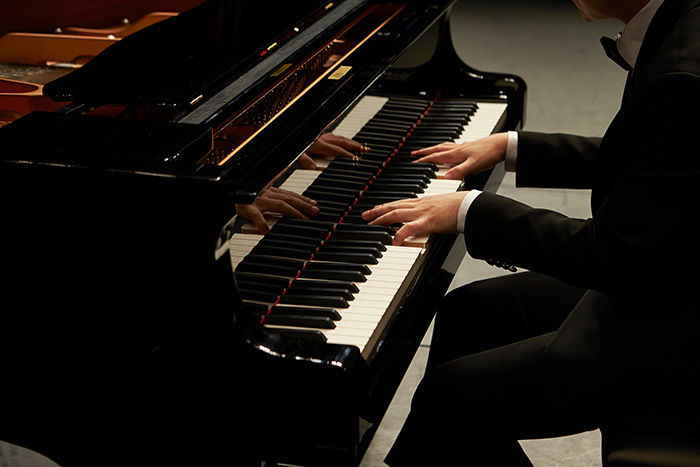 Man in suit playing grand piano feat