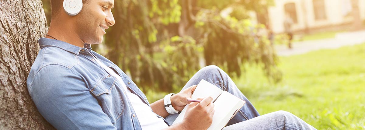 Man wearing headphones sitting outside writing music