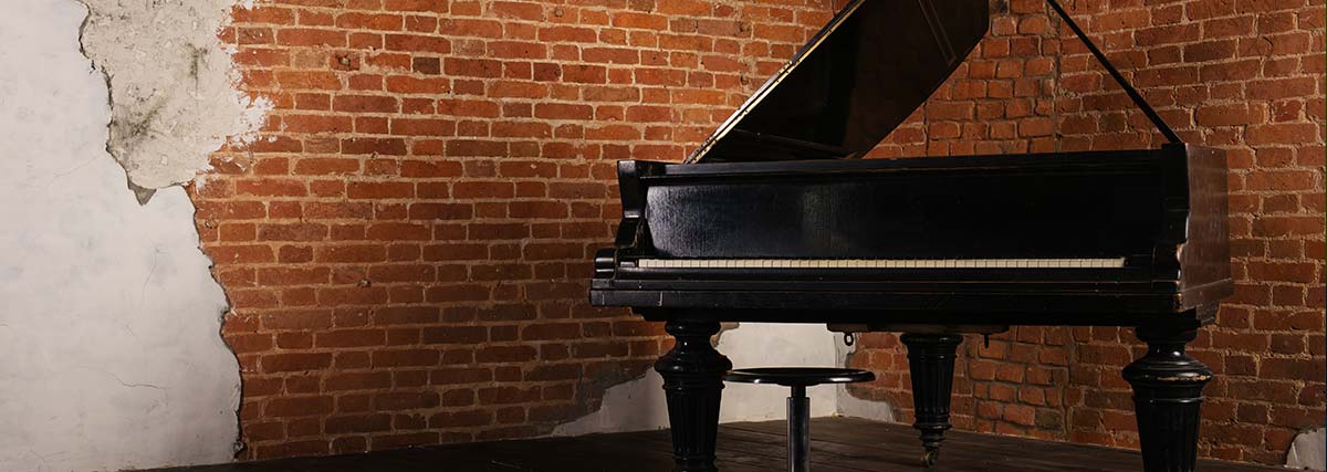 Old grand piano inside a room with brown color brick wall