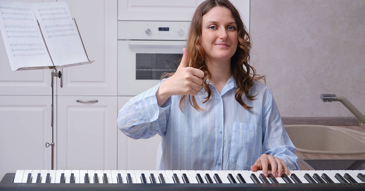 Smiling woman doing an OK hand sign while the other hand is pressing on the piano keyboard