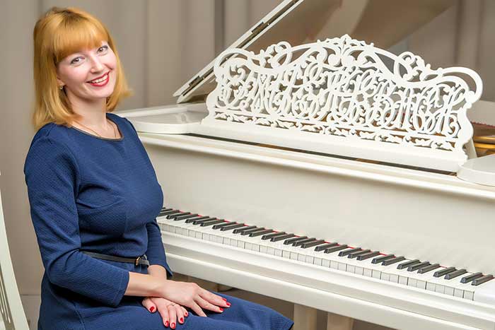 woman in red sitting in front of a white grand piano feat